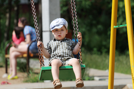 Handsome little boy in cap swings on children playground at summer dayの写真素材