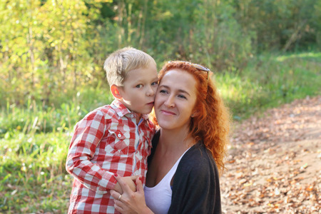 Handsome little son kisses his young mother in autumn park at sunny dayの写真素材