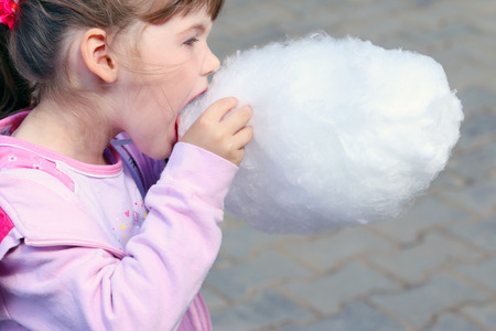 Little beautiful girl in pink eats cotton candy outdoor at summer dayの写真素材