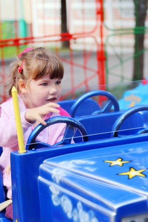 Little pretty girl rides on bright car in amusement park at summer dayの写真素材