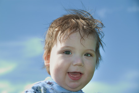 Close up view of happy little cute baby at background of blue sky at sunny dayの写真素材
