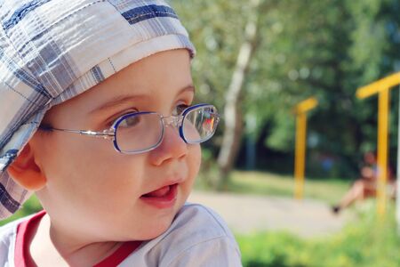 Little cute boy in glasses and cap looks away and smiles at summer dayの写真素材