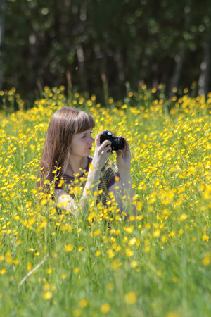 Pretty woman shoots among yellow flowers at meadow at summer dayの写真素材