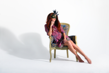 Seated in armchair beautiful young girl in short dress with black mask looking awayの写真素材