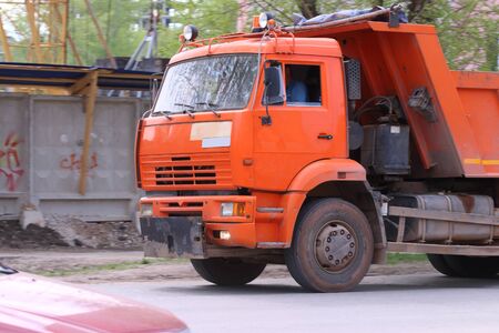 Close up of orange bright truck moving to construction site at spring day