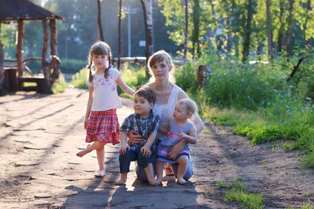 Happy mother with three little barefoot children pose in summer sunny parkの写真素材