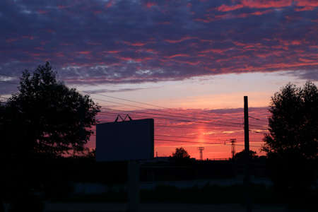 Beautiful sky during red sunset, clouds and silhouettes of trees, billboard and wiresの写真素材
