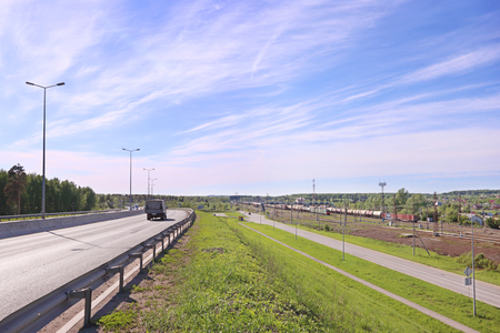 Freight train on railway station and car moves on asphalt road on hillの写真素材