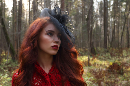 Pretty girl in black retro hat looks away in autumn forest at warm sunny dayの写真素材