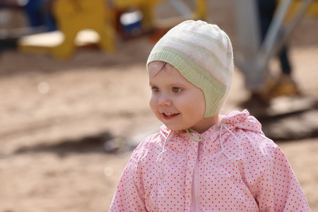 Little cute happy girl in hat walks on playground at sunny spring dayの写真素材