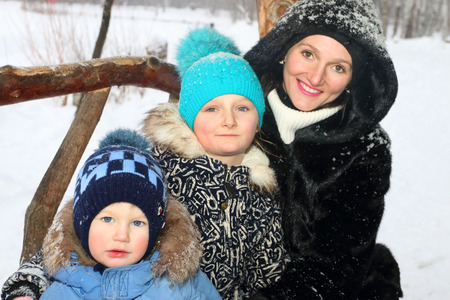 Happy mother with son, daughter smile in winter day during snowfall, focus on girlの写真素材