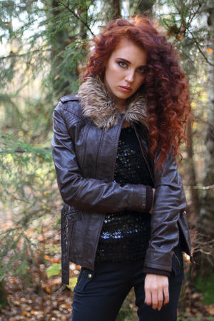 Girl with curly hair in leather jacket stands in sunny autumn forest, shallow dofの写真素材