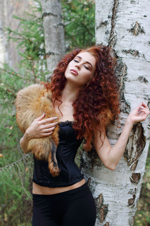 Beautiful woman in corset with fur dreams near birch in autumn forestの写真素材