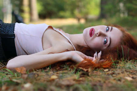 Beautiful girl lies on dry leaves and looks at camera in autumn forestの写真素材