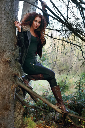 Happy woman in boots with curly hair poses on old fir-tree in forestの写真素材