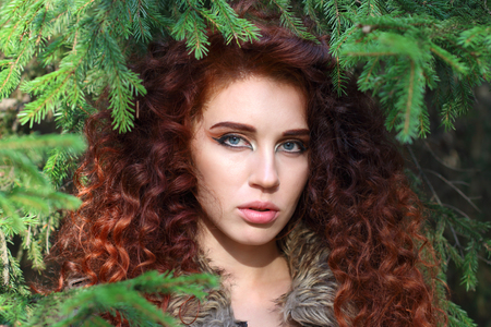 Beautiful young woman poses among fir branches in forest, shallow dofの写真素材