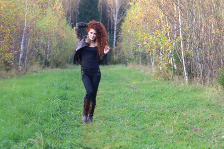 Pretty young woman in leather jacket stands on grass in autumn forestの写真素材