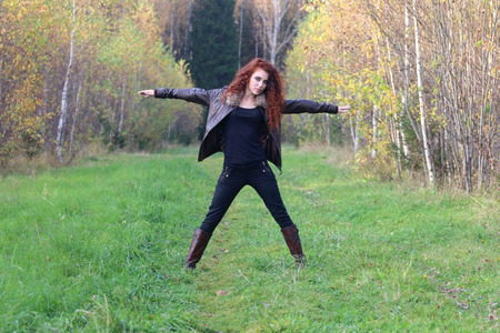 Pretty young woman in leather jacket poses on grass in autumn forestの写真素材