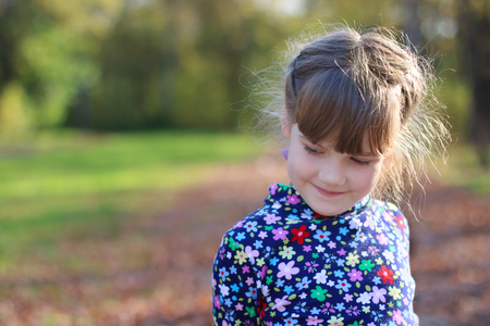Cute little girl smiles and looks away in sunny green park, shallow dof, close upの写真素材