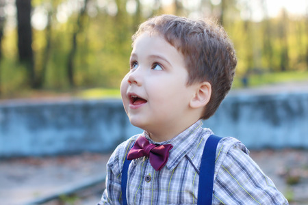 Handsome little boy with bow tie looks up in sunny park, shallow dofの写真素材