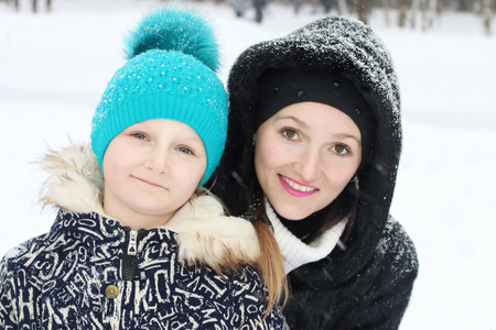 Happy mother with her daughter embrace in winter day during snowfallの写真素材