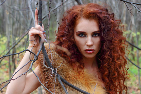Pretty young woman poses among tree branches in autumn forestの写真素材