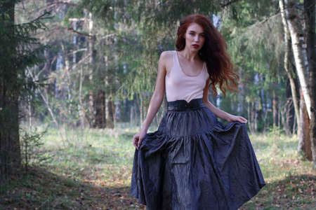 Young cute woman in skirt and belt poses on wind in sunny autumn forestの写真素材