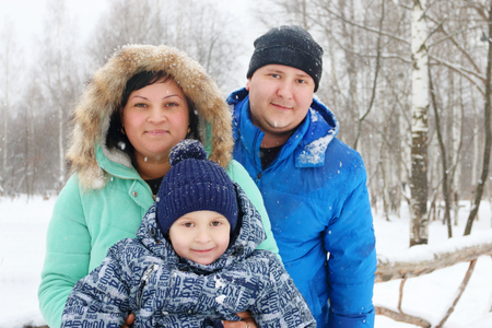 Happy family (mother, father, son) pose during snowfall in winter day, focus on boyの写真素材