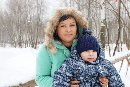 Happy mother with her little son during snowfall in winter day, focus on womanの写真素材
