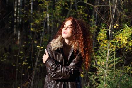 Young pretty woman in jacket with closed eyes basks in sun in forestの写真素材