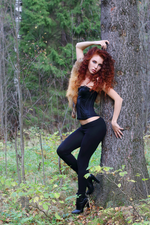 Beautiful girl in black brace poses near big tree in autumn forestの写真素材