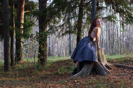 Beautiful girl sits on big stump and poses on wind in autumn forestの写真素材