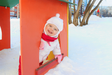 Happy little girl plays in bright small house on playground at winter sunny dayの写真素材