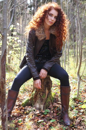Beautiful girl in boots sitting on tree stump in sunny autumn forestの写真素材