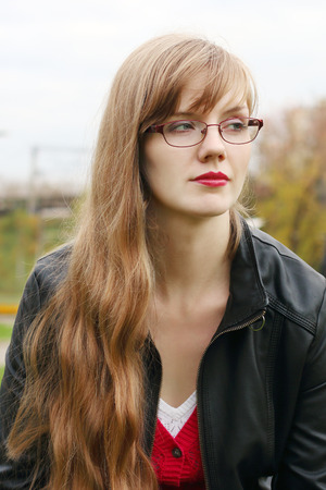 Beautiful woman in glasses in leather jacket looks away outdoorの写真素材