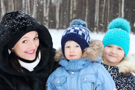 Happy mother with son, daughter pose in winter day during snowfallの写真素材