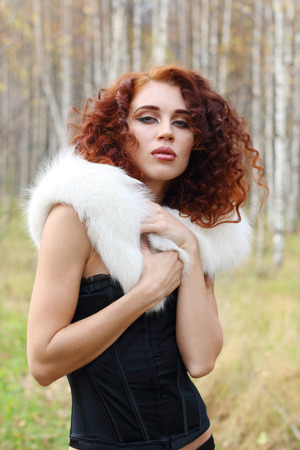 Beautiful woman in corset with white fur poses in autumn forestの写真素材