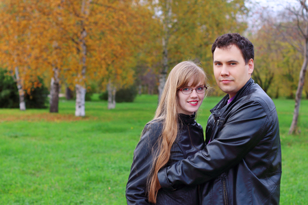 Man embraces woman in black leather jackets in autumn parkの写真素材
