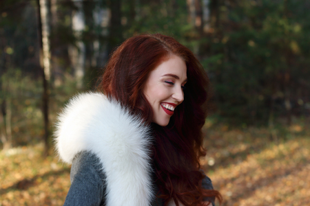 Pretty girl with make up and white fur laughs in forest at sunny dayの写真素材