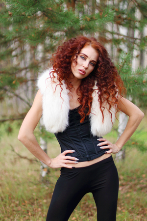 Pretty woman in corset with white fur and curly hair poses in pine forestの写真素材