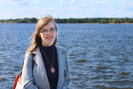 Woman in jacket and glasses stands near river at sunny summer dayの写真素材