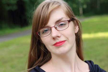 Beautiful woman in glasses poses in sunny green park at summerの写真素材