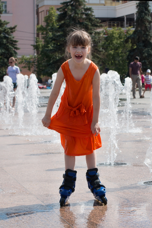 Happy girl in wet dress roller skates in fountain in summer cityの写真素材