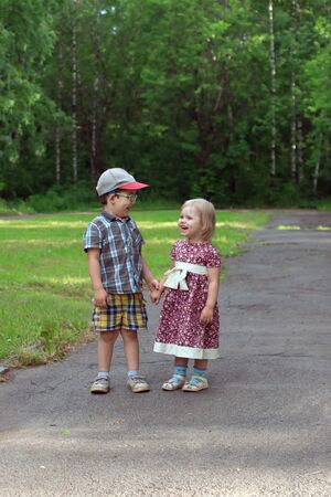 Little pretty girl and boy laugh and hold hands in park at sunny dayの写真素材