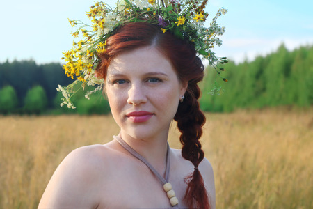 Beautiful freckled woman in wreath in dry field at summer dayの写真素材