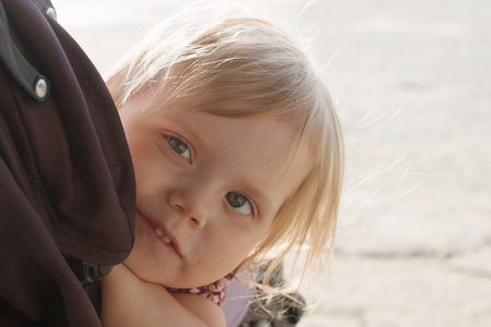 Little smiling blonde girl looks out pram outdoor, closeup, shallow dofの写真素材