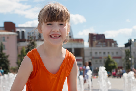 Happy girl in wet dress laughs near dry fountain in summer city at sunny dayの写真素材