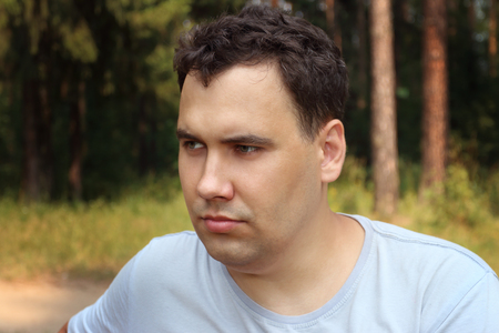 Sad man looks away and thinks at sunny summer forest, shallow dofの写真素材