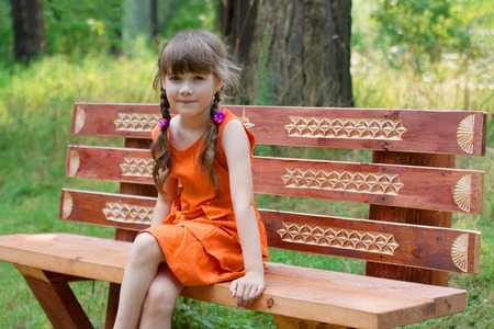 Happy cute little girl in orange sits on wooden beanch at summer dayの写真素材
