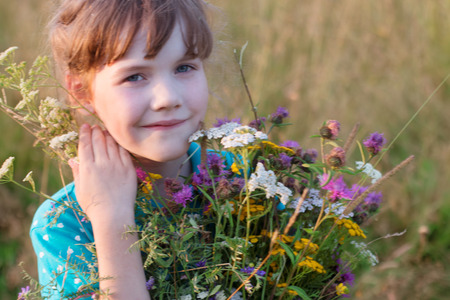Happy little girl holds wild flowers and smiles in dry field at summer dayの写真素材